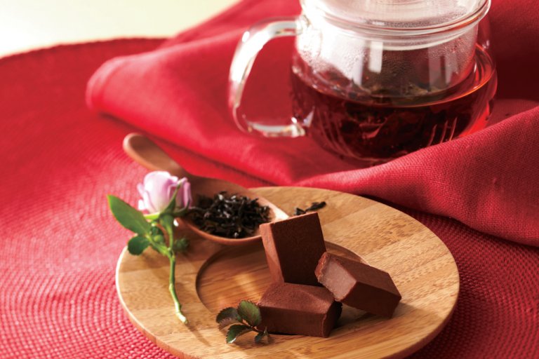 A plate of chocolate near a pot of tea.
