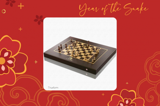 A white square frame at the center of a red floral background with a brown chess board in the middle. The words "Year of the Snake" are at the top and "Trueform" is at the bottom.