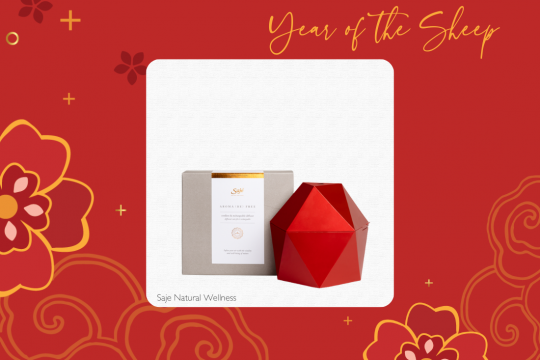 A white square frame at the center of a red floral background, with an image of a geometric red essential oil diffuser. The text at the top says "Year of the Sheep" and the text at the bottom says "Saje Natural Wellness."